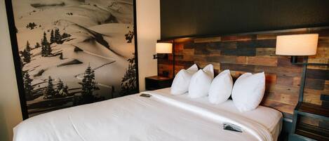 A hotel room with a large bed, a wooden headboard, and a wall mural of a snowy mountain landscape.