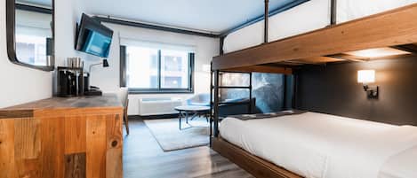 A modern, compact room with a bunk bed, a desk with a flat-screen TV, and a seating area with a table and chairs.