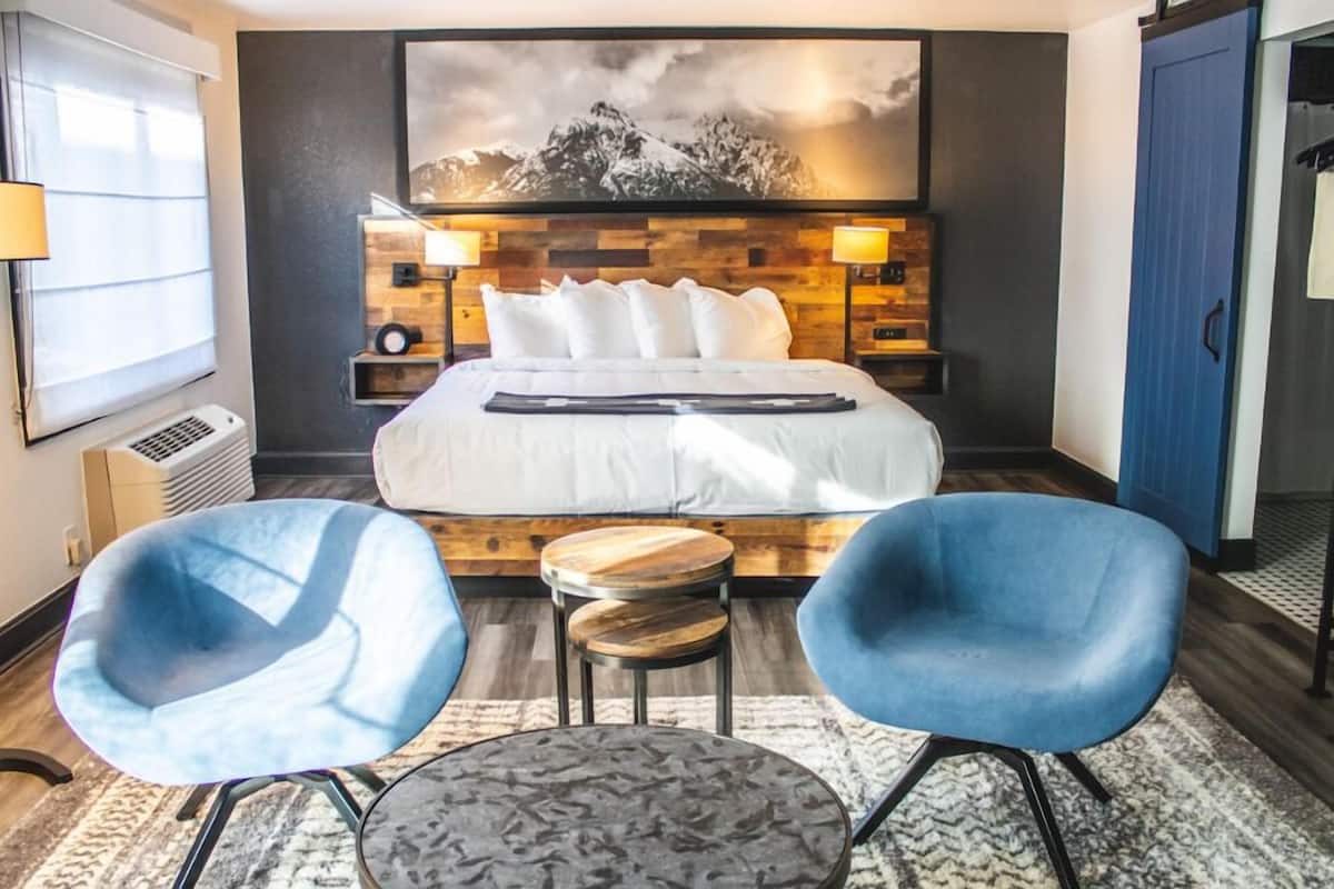 Ein Hotelzimmer mit einem großen Bett, zwei blauen Stühlen, einem kleinen runden Tisch, einem an der Wand befestigten Fernseher und einem Bergpanorama.