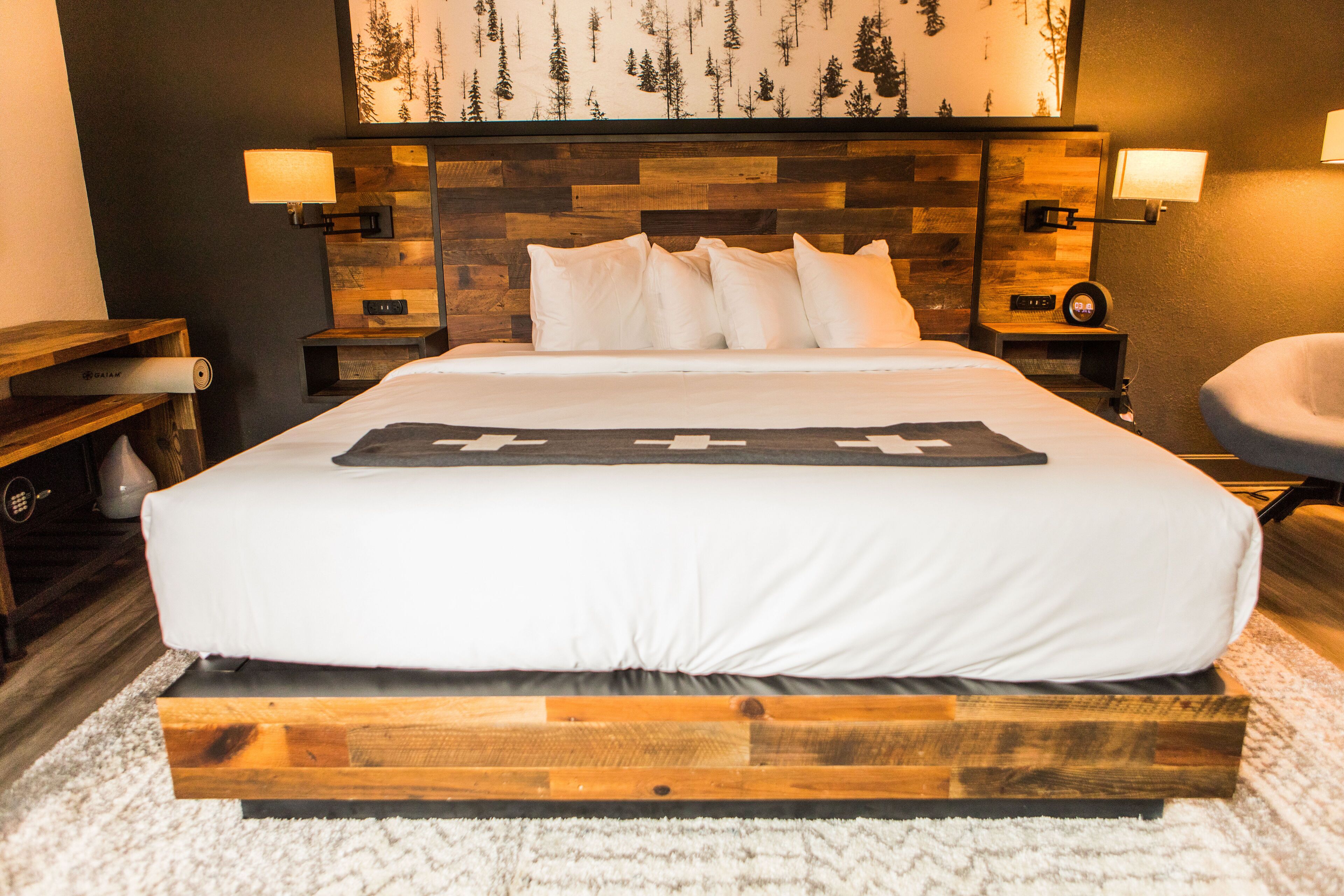 A neatly made bed with a wooden headboard, two bedside lamps, and a wall-mounted clock.