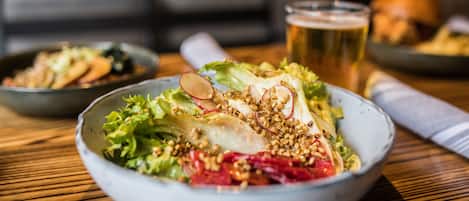 Ensalada con diferentes ingredientes, una jarra de cerveza y una servilleta sobre una mesa de madera.