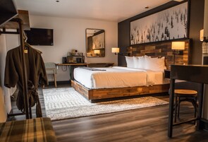Una habitación de hotel moderna con una cama de madera, un escritorio, una silla, una bata y un cuadro grande en la pared.