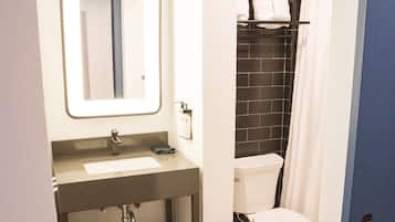 Baño con lavamanos, espejo y retrete blancos, e igualmente una zona de ducha con azulejos negros.