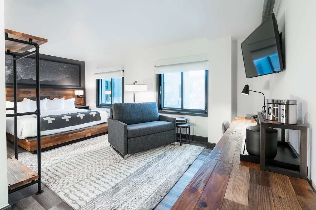 Ein modernes Hotelzimmer mit Bett, Sofa, Fernseher und Schreibtisch mit Lampe und Kaffeemaschine.