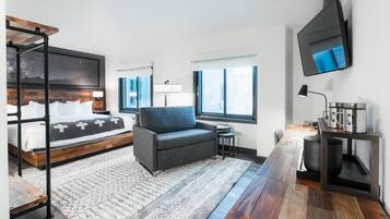 Ein modernes Hotelzimmer mit Bett, Sofa, Fernseher und Schreibtisch mit Lampe und Kaffeemaschine.