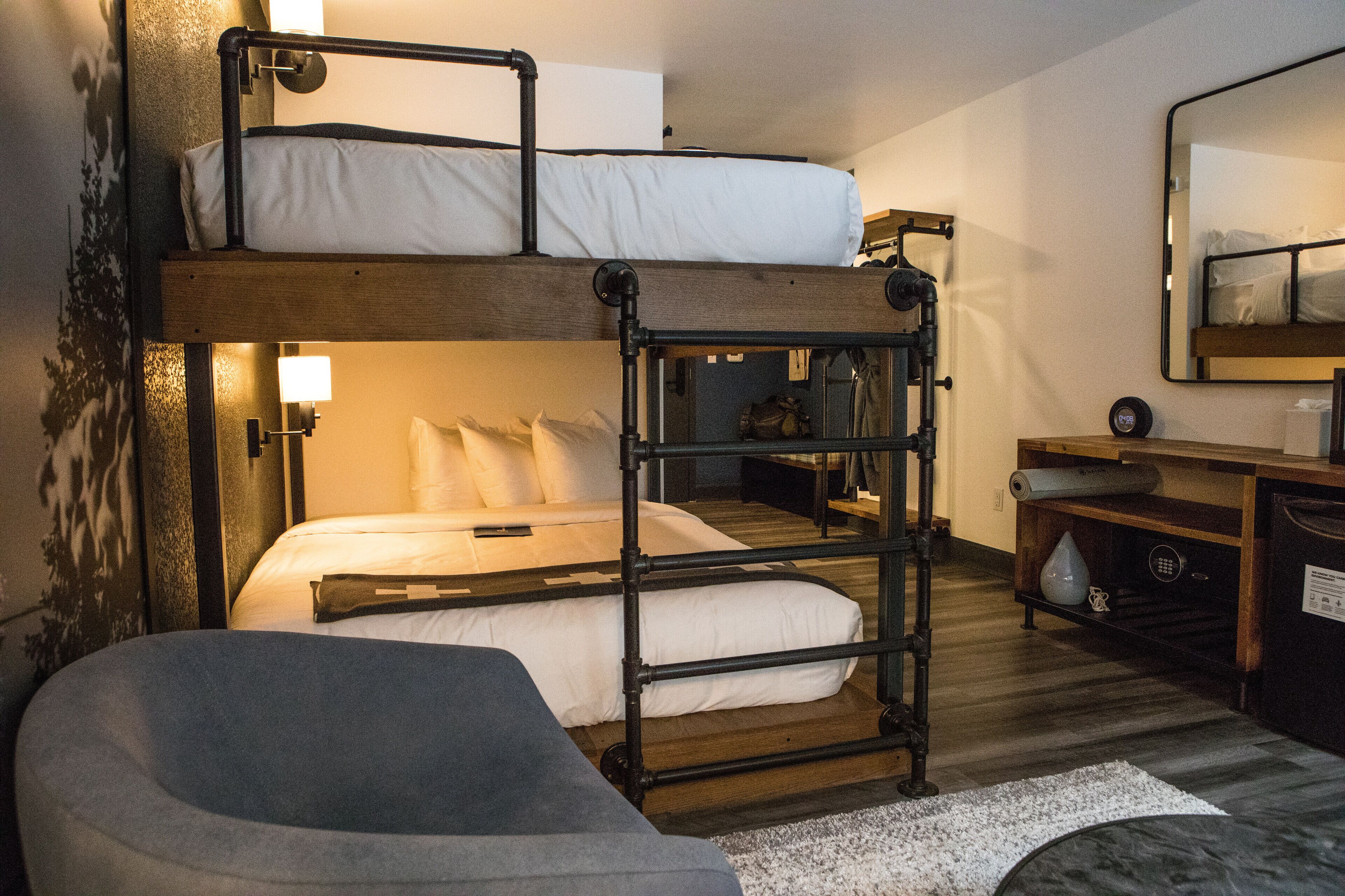 A bunk bed room with a desk and chair, a mirror, and a small shelf.