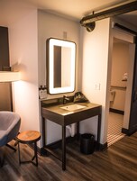 Un baño de hotel pequeño con espejo, lavabo y un taburete.