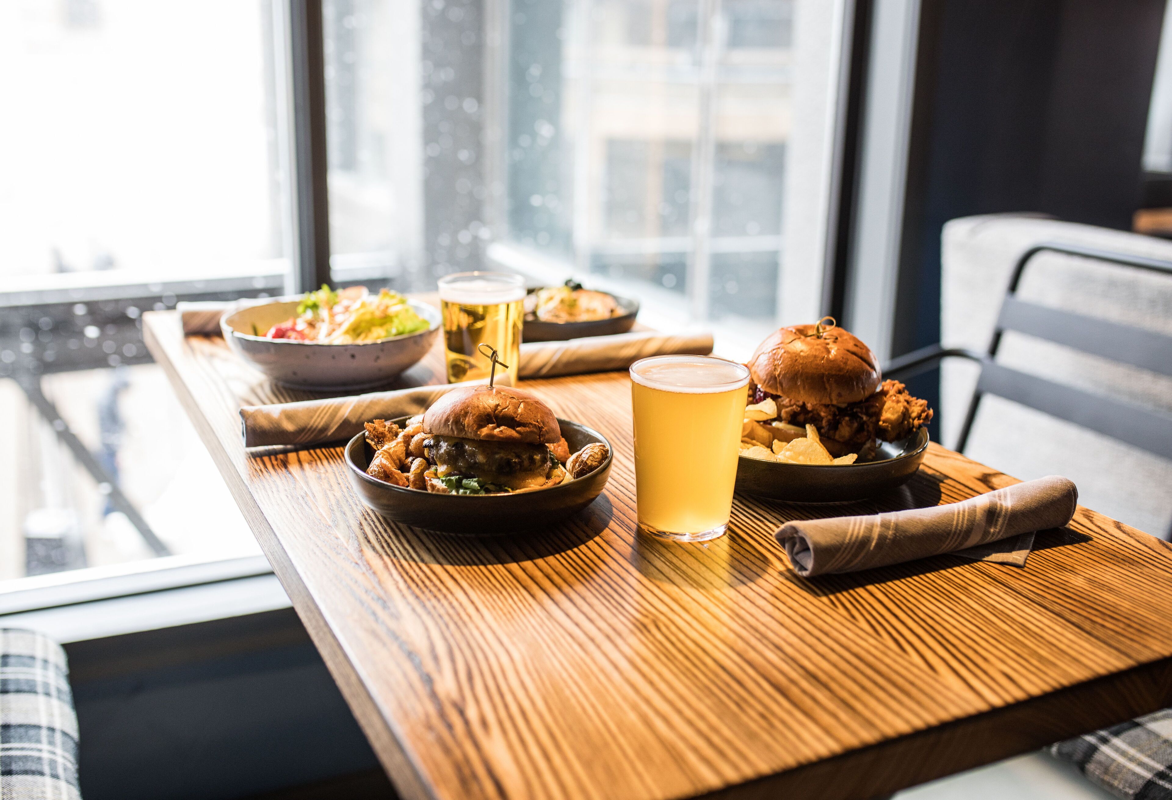 Una mesa de comedor con una hamburguesa, un tazón de ensalada y una jarra de cerveza.