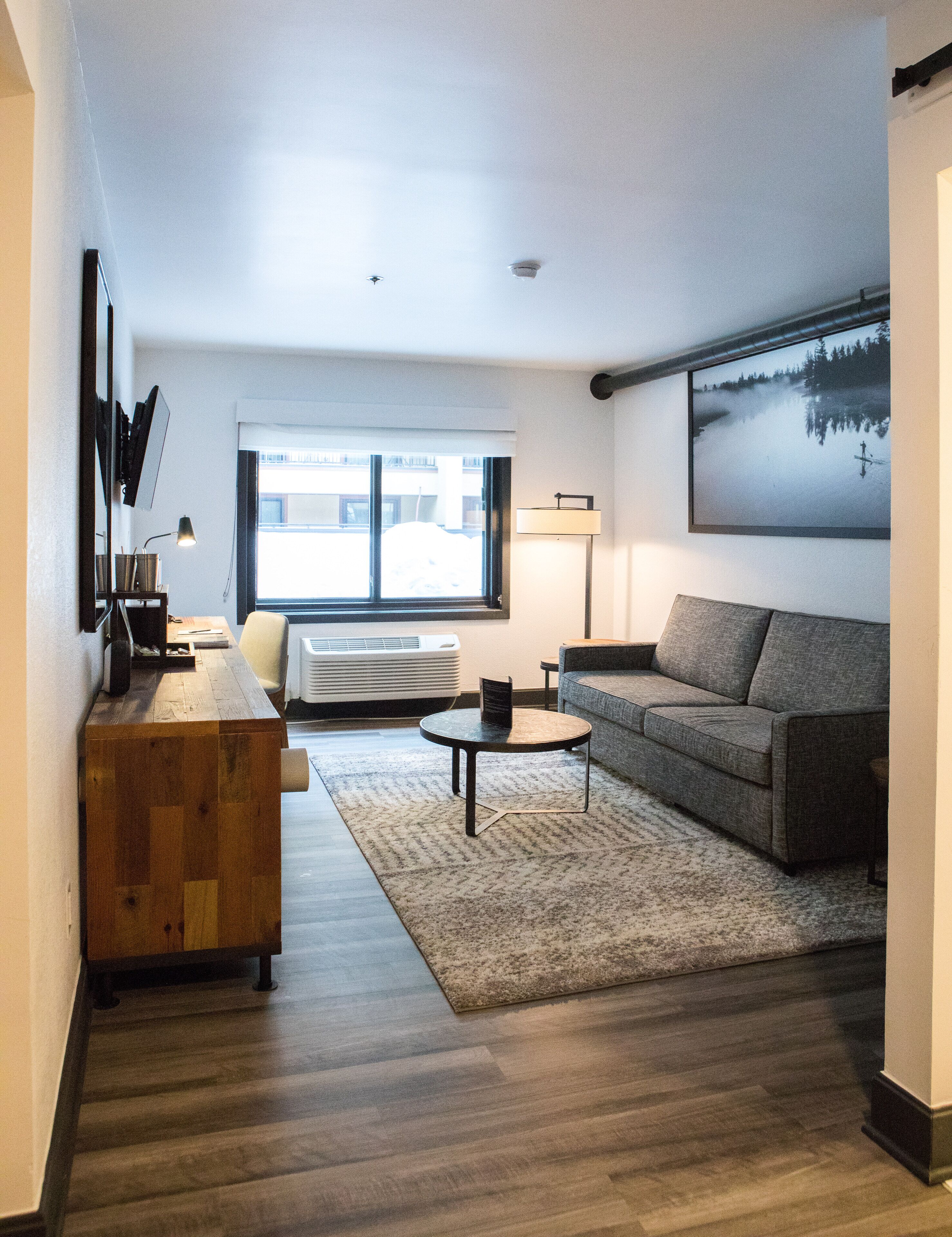 A modern living room with a grey sofa, a wooden coffee table, and a large window.