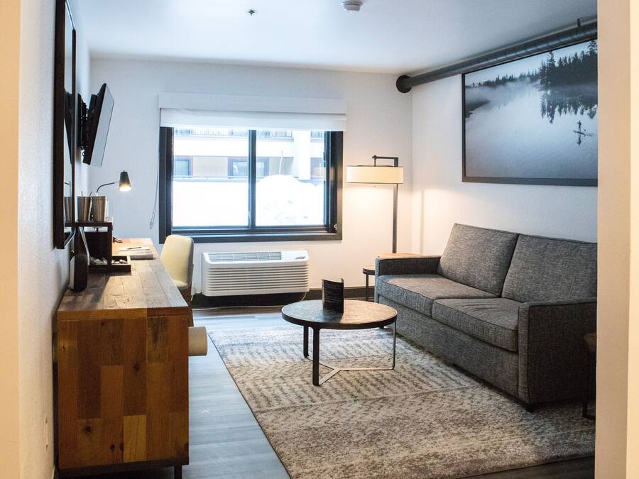 A modern living room with a grey sofa, a wooden coffee table, and a large window.