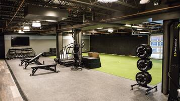 A gym with weightlifting equipment, a treadmill, and a green turf area.