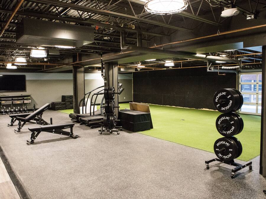 A gym with weightlifting equipment, a treadmill, and a green turf area.