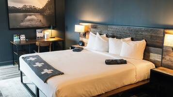 A neatly made bed with white linens, a wooden headboard, and a desk with a lamp.