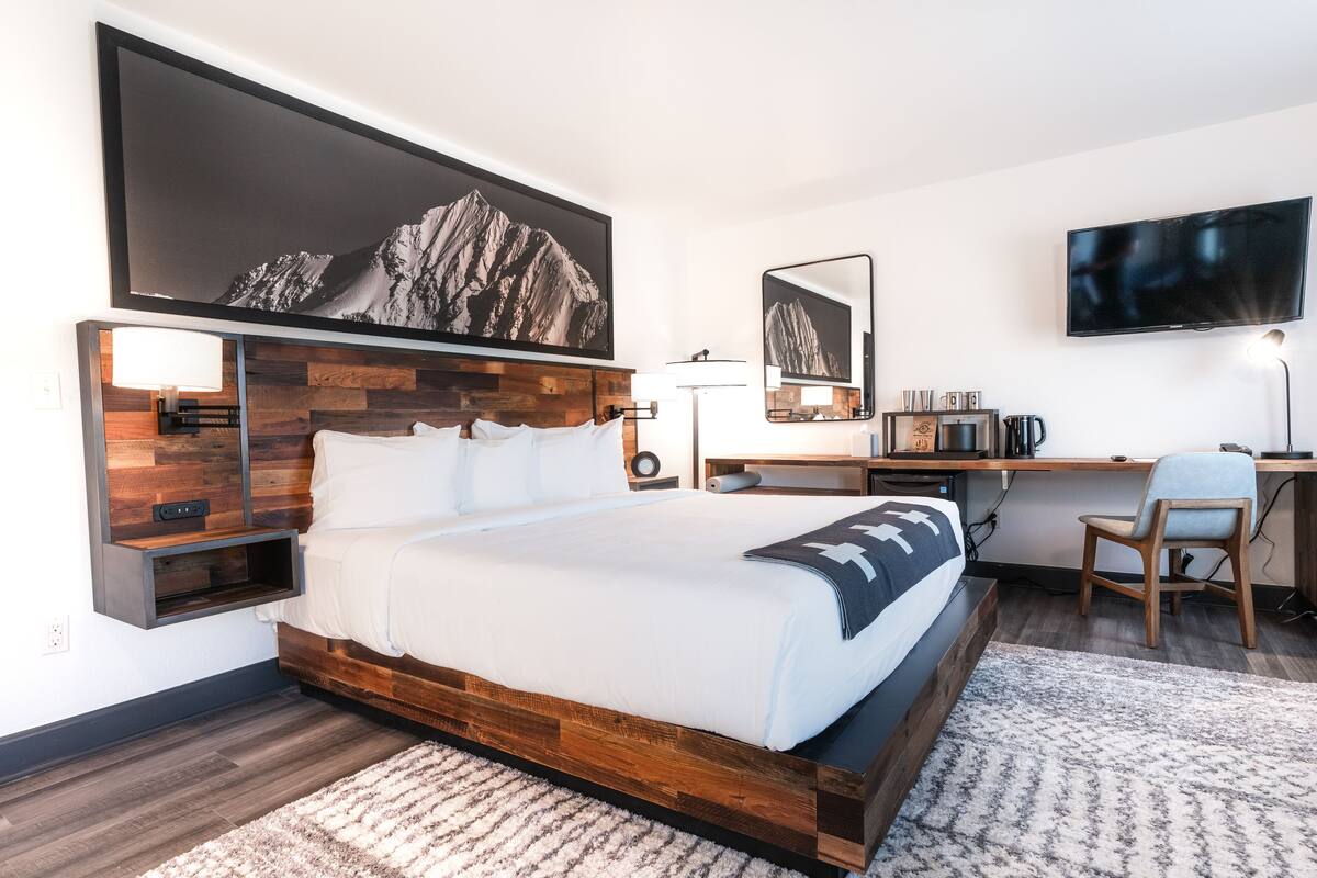 Ein modernes Schlafzimmer mit einem großen Bett, einem Schreibtisch, einem Sessel und einem Fernseher.