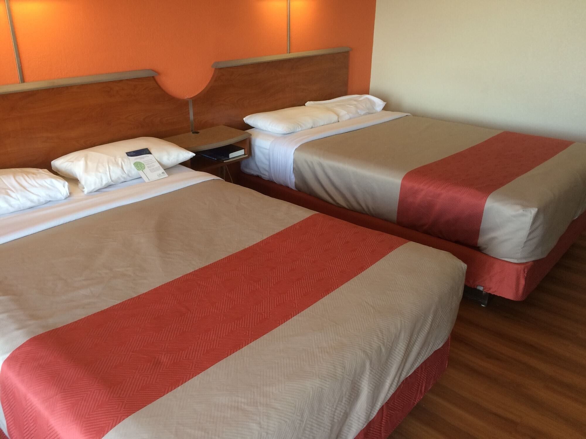 Two beds with red and beige bedding, wooden headboards, and a nightstand with a lamp.