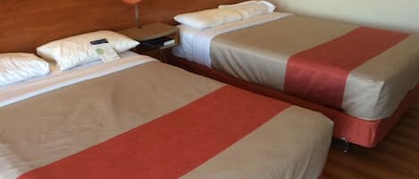 Two beds with red and beige bedding, wooden headboards, and a nightstand with a lamp.