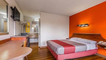 Habitación de hotel con piso de madera, cama con cubrecama rojo y gris, cabecera de madera, mesita de noche con teléfono y espejo en la pared.
