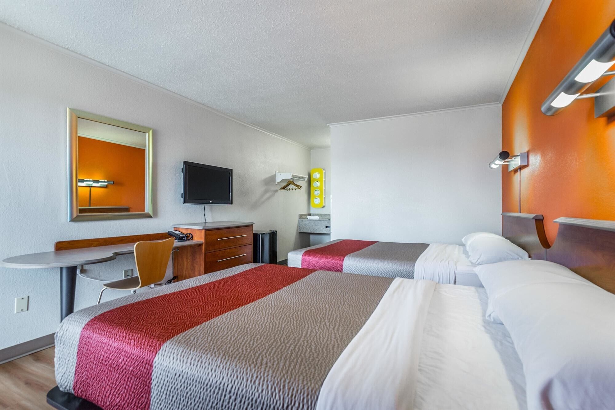 Camera d'albergo con due letti, una scrivania con sedia, televisione e uno specchio.