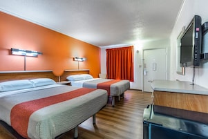 Habitación de hotel con dos camas, un escritorio, un televisor y la puerta del baño.
