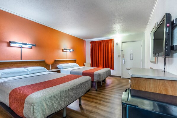 A hotel room with two beds, a desk, a TV, and a bathroom door.