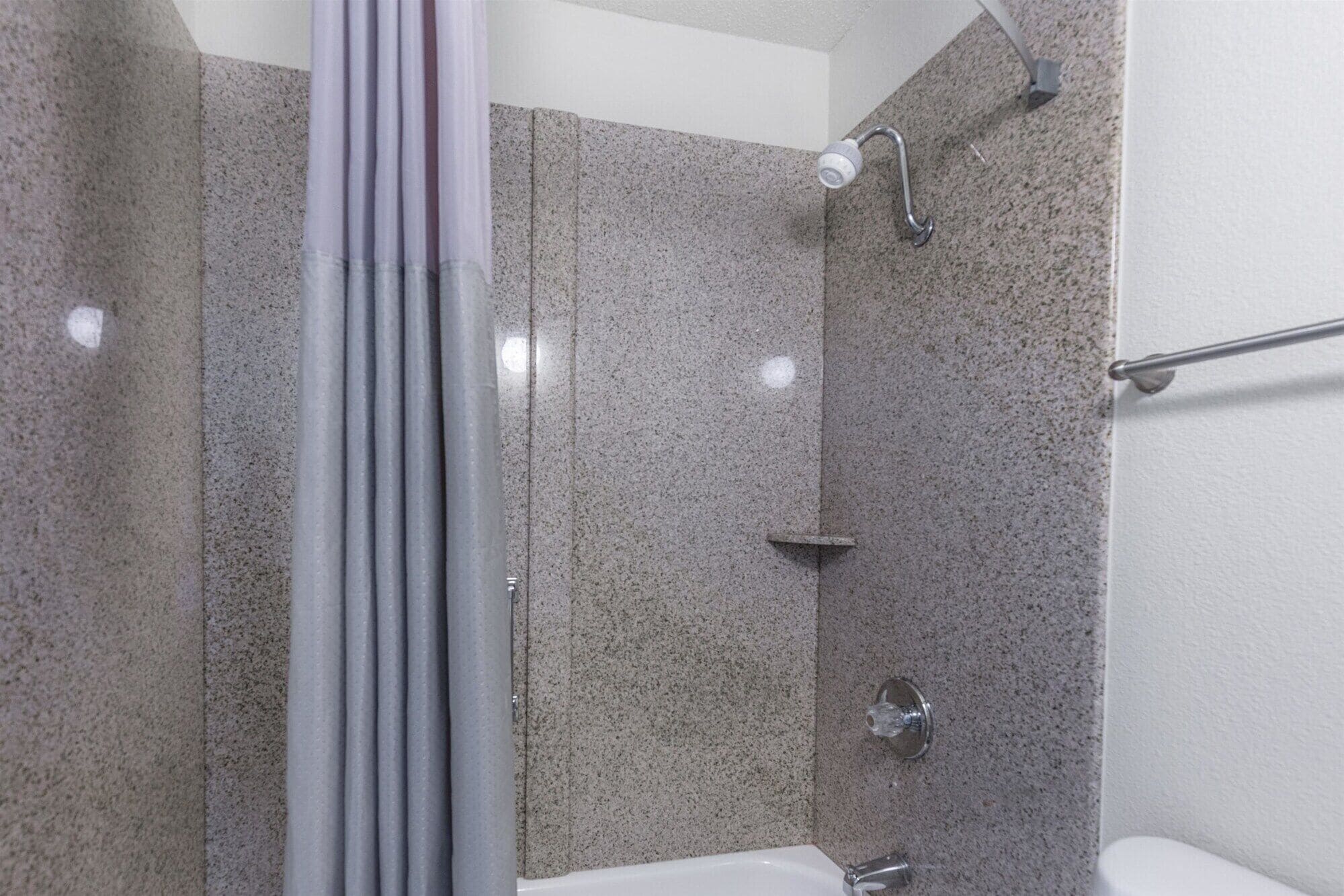 A shower with a glass door, a handheld showerhead, and a wall-mounted faucet.