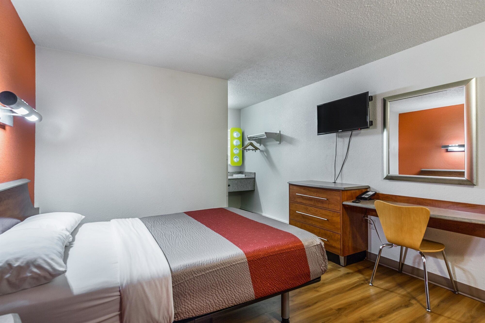 Een hotelkamer met een bed, een bureau met stoel, een televisie en een spiegel.
