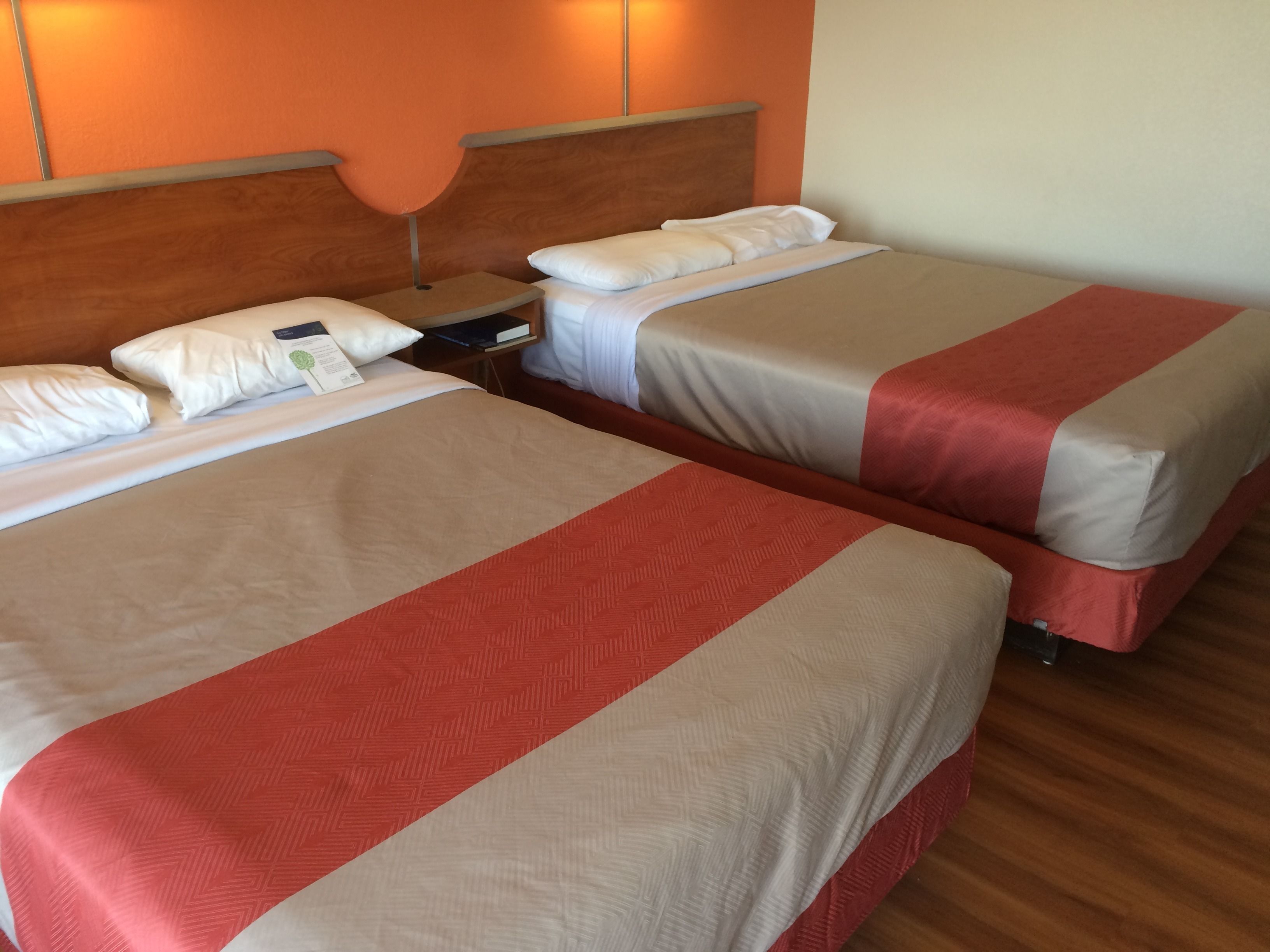 Dos camas con cabeceros de madera, una mesita de noche y una lámpara fijada a la pared.