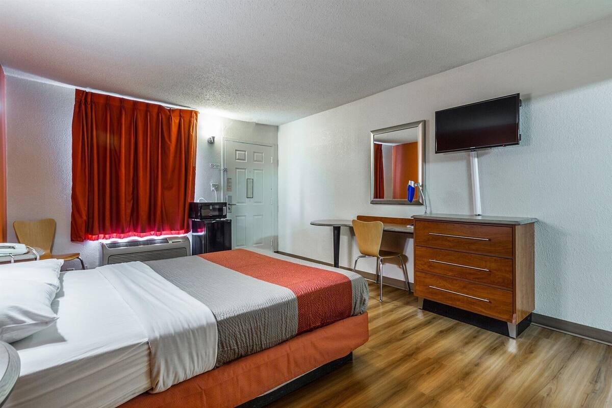 A hotel room with a bed, a desk, a chair, a television, and a microwave.
