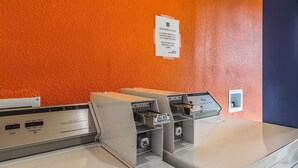 A self-service laundry station with multiple washing machines, a price tag of $1.50, and a sign indicating guest services at the lobby. - Motel 6 Mount Vernon, IL (Mount Vernon)