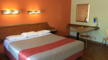 Habitación de hotel con una cama grande, dos lámparas fijadas a la pared, un escritorio con silla y un espejo en la pared.