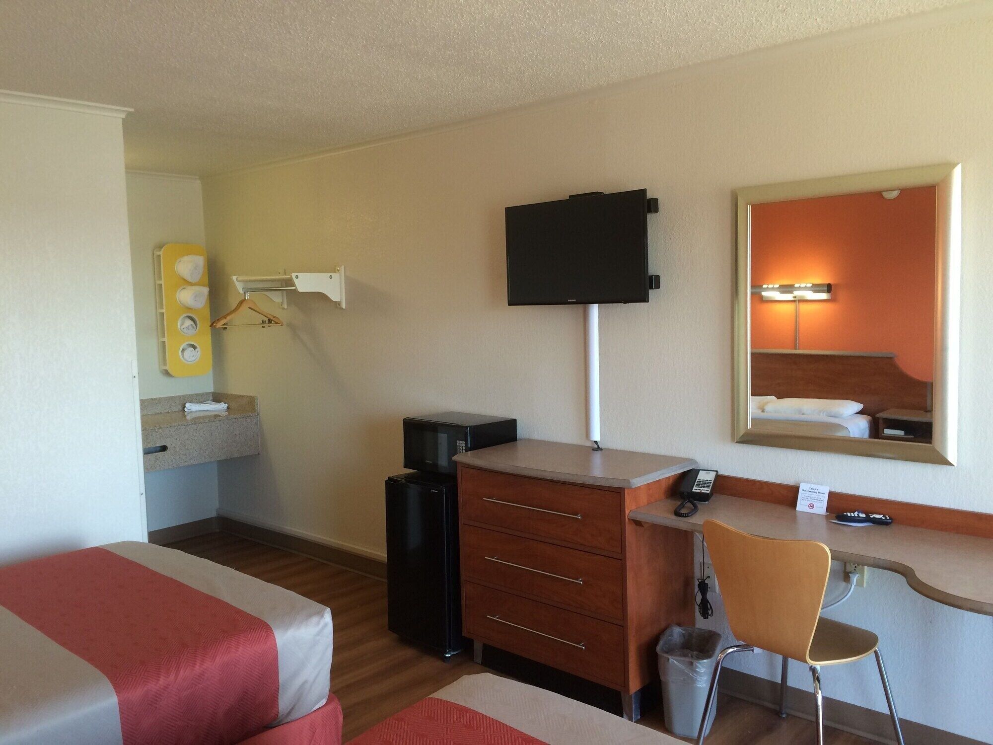 Habitación de hotel con cama, escritorio, silla, televisión, microondas y cubo de basura.