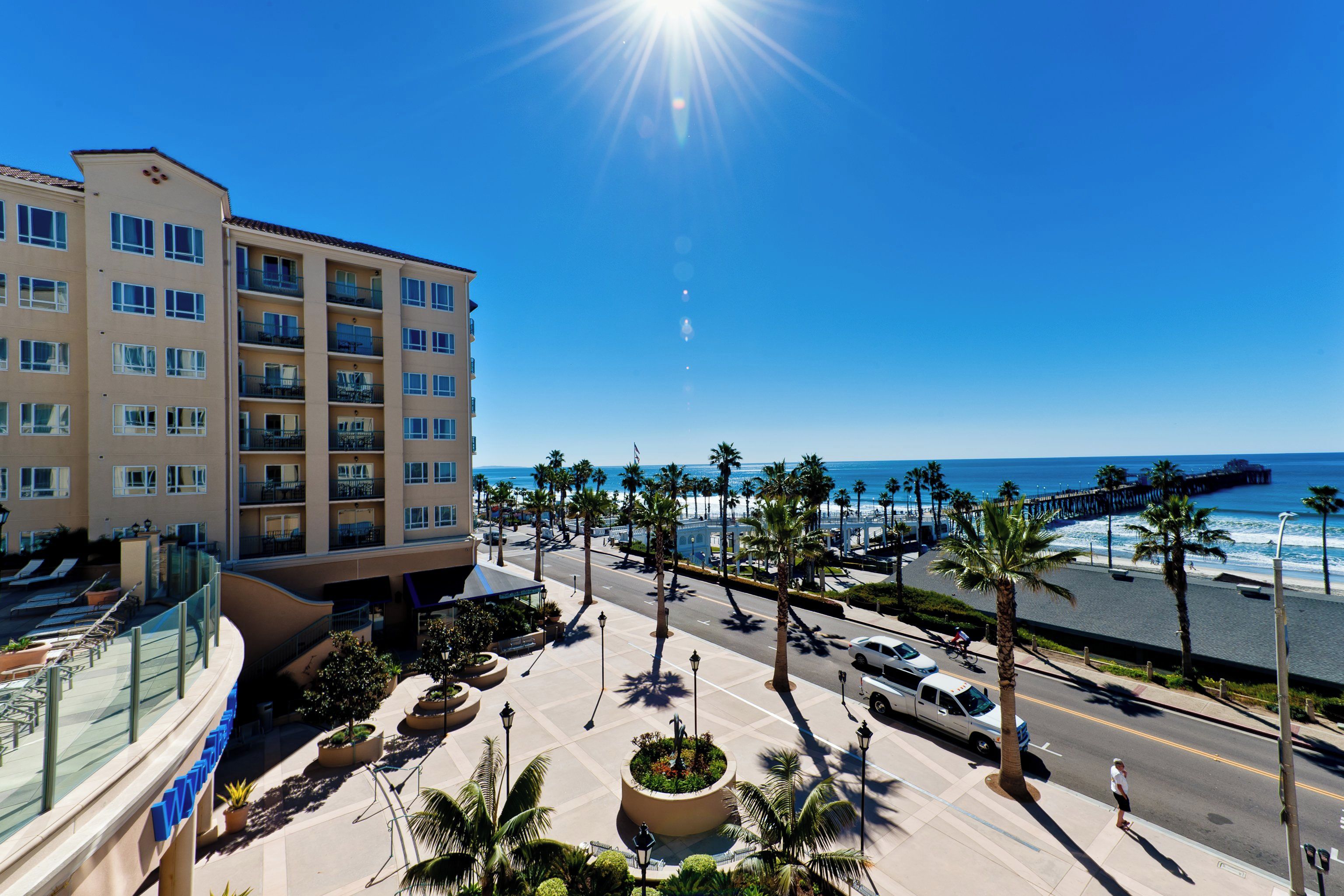 A hotel with multiple floors, a beachfront view, and a promenade with palm trees.