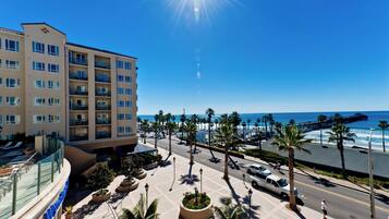 A hotel with multiple floors, a beachfront view, and a promenade with palm trees.