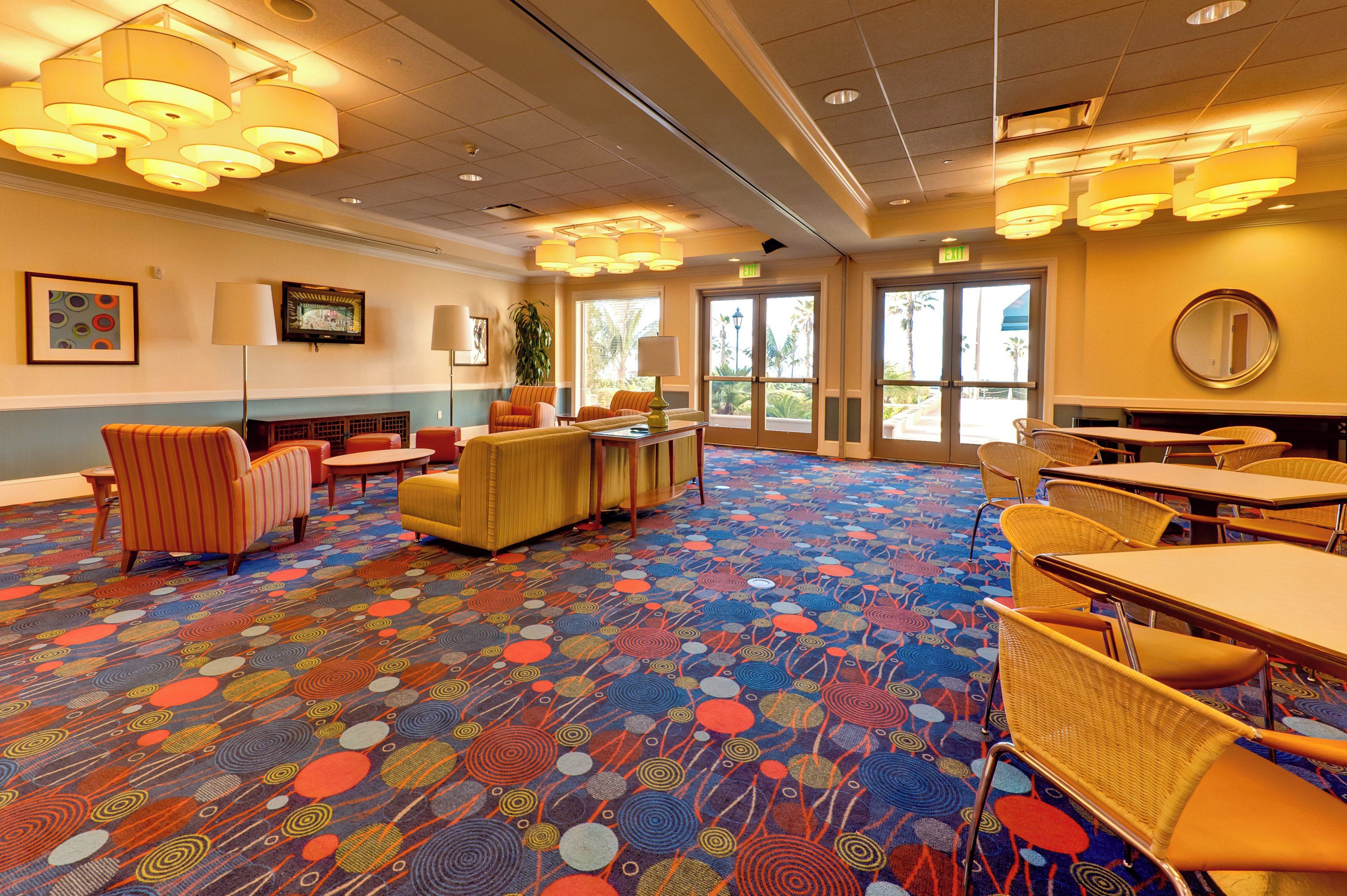 Un hall d’hôtel avec un tapis aux couleurs vives, des coins salon et un téléviseur fixé au mur.