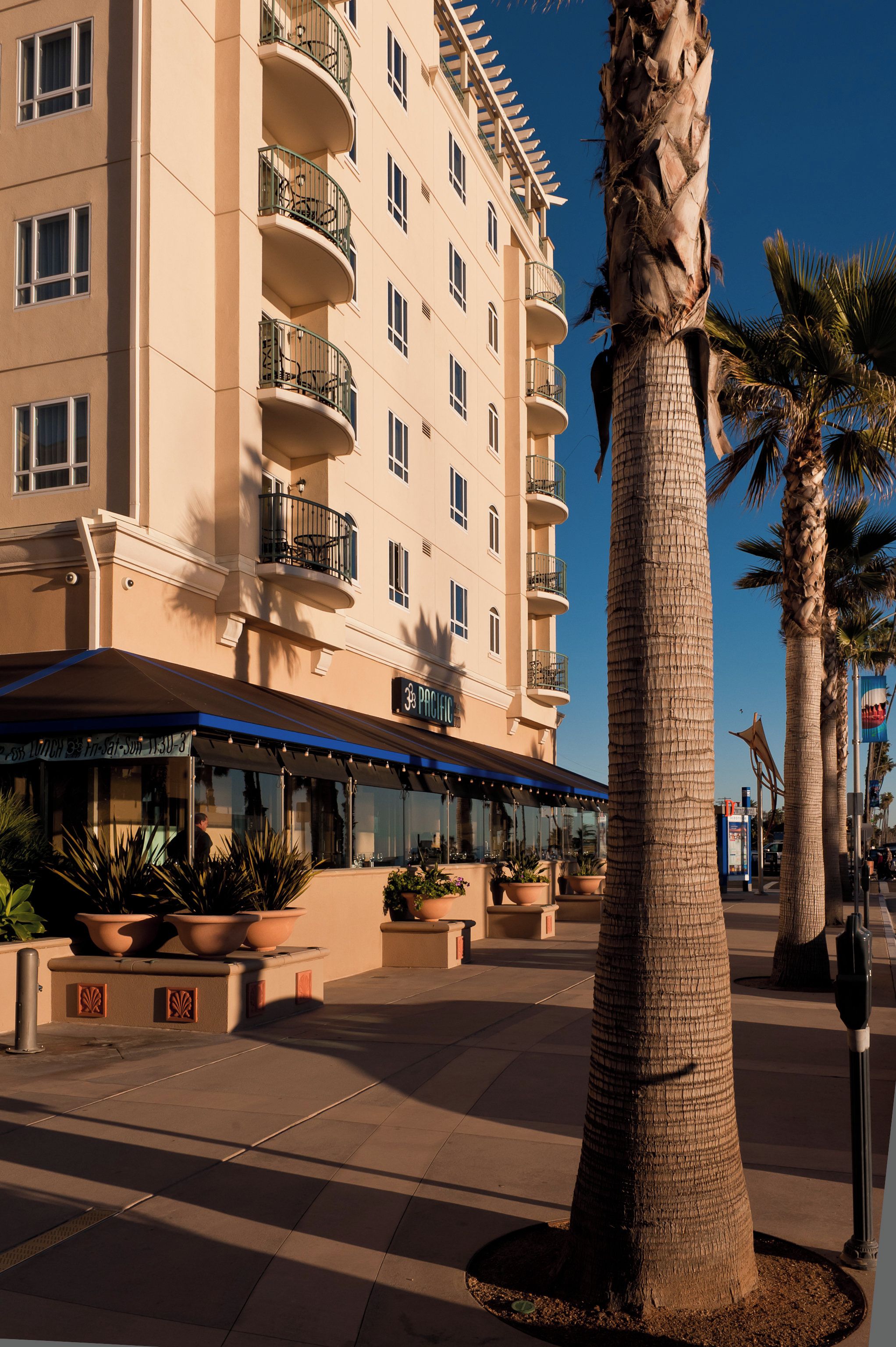 A multi-story hotel with balconies, a covered outdoor seating area, and palm trees.