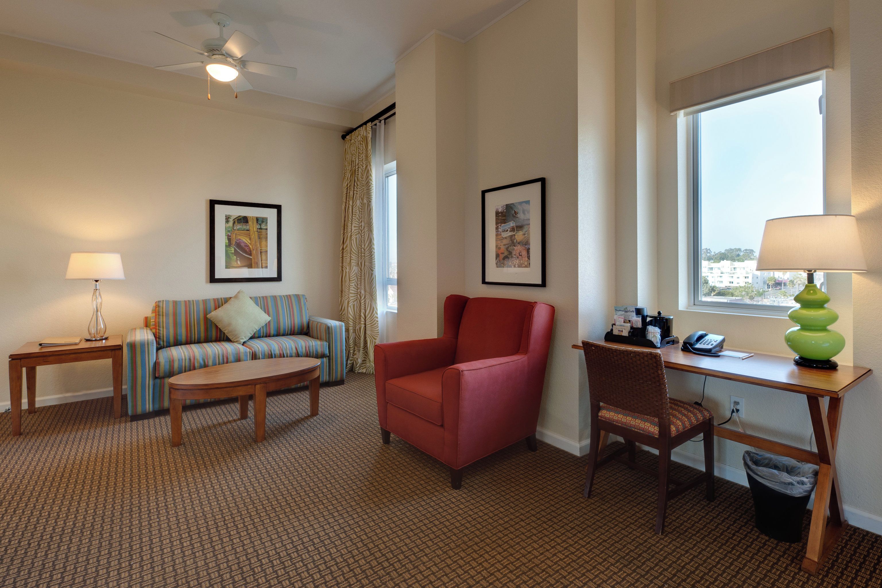 A hotel room with a sofa, armchair, desk, and a window with a view.