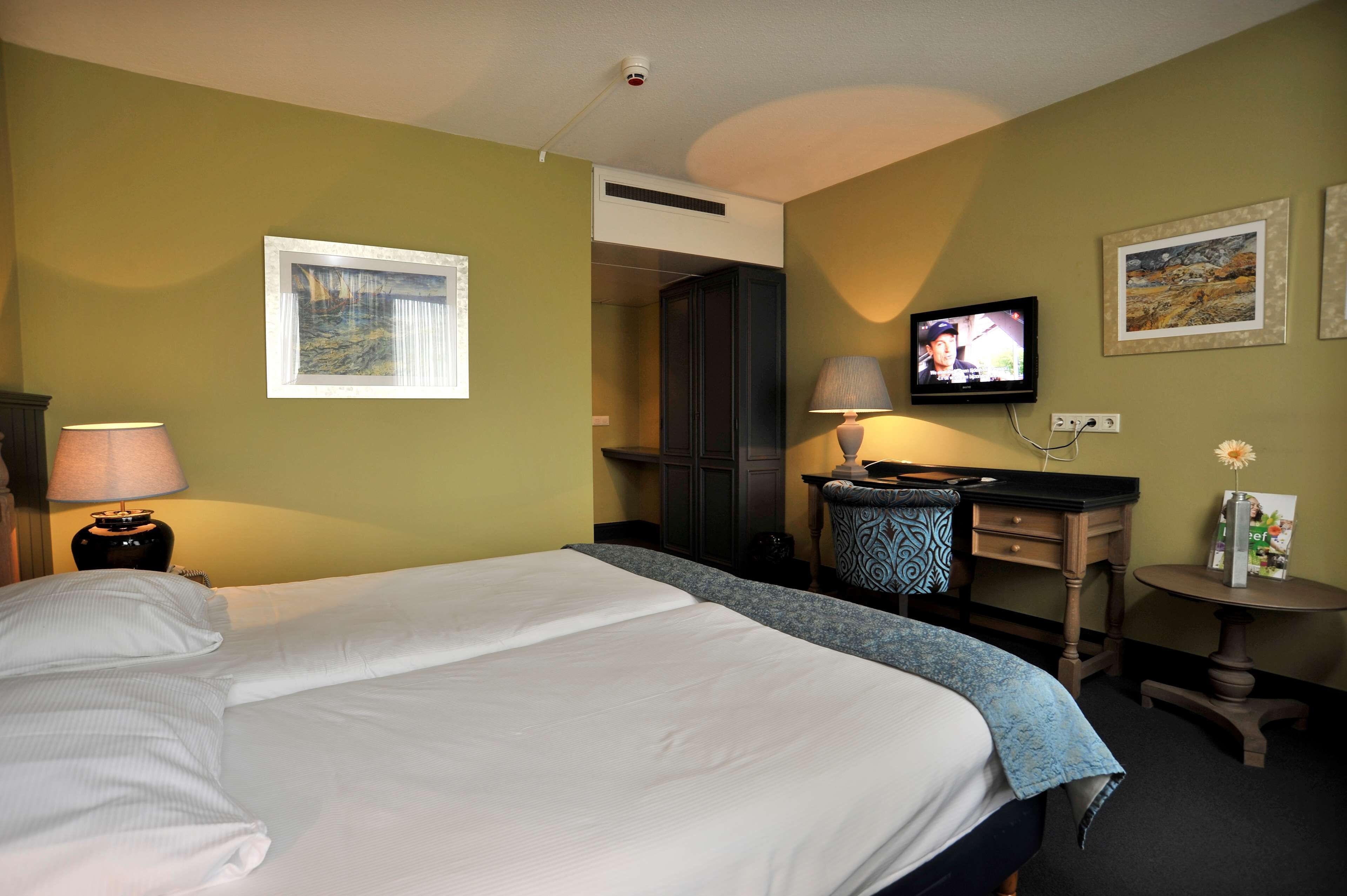 A hotel room with a bed, a desk with a computer, a television, and a window with blinds.