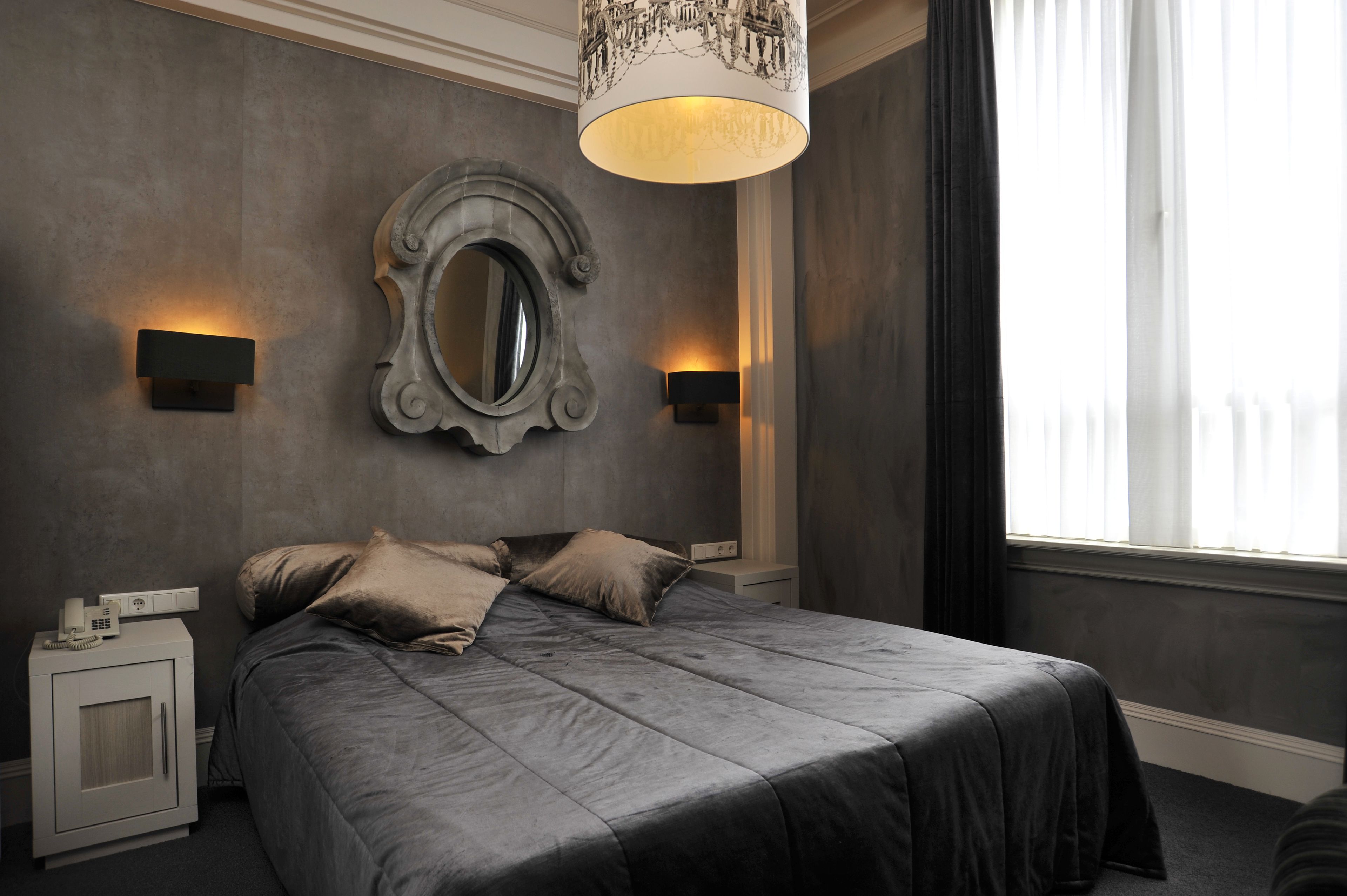 A modern bedroom with a large bed, two bedside lamps, a decorative mirror, and a window with curtains.