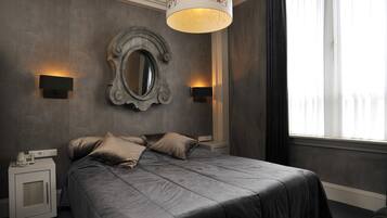 A modern bedroom with a large bed, two bedside lamps, a decorative mirror, and a window with curtains.