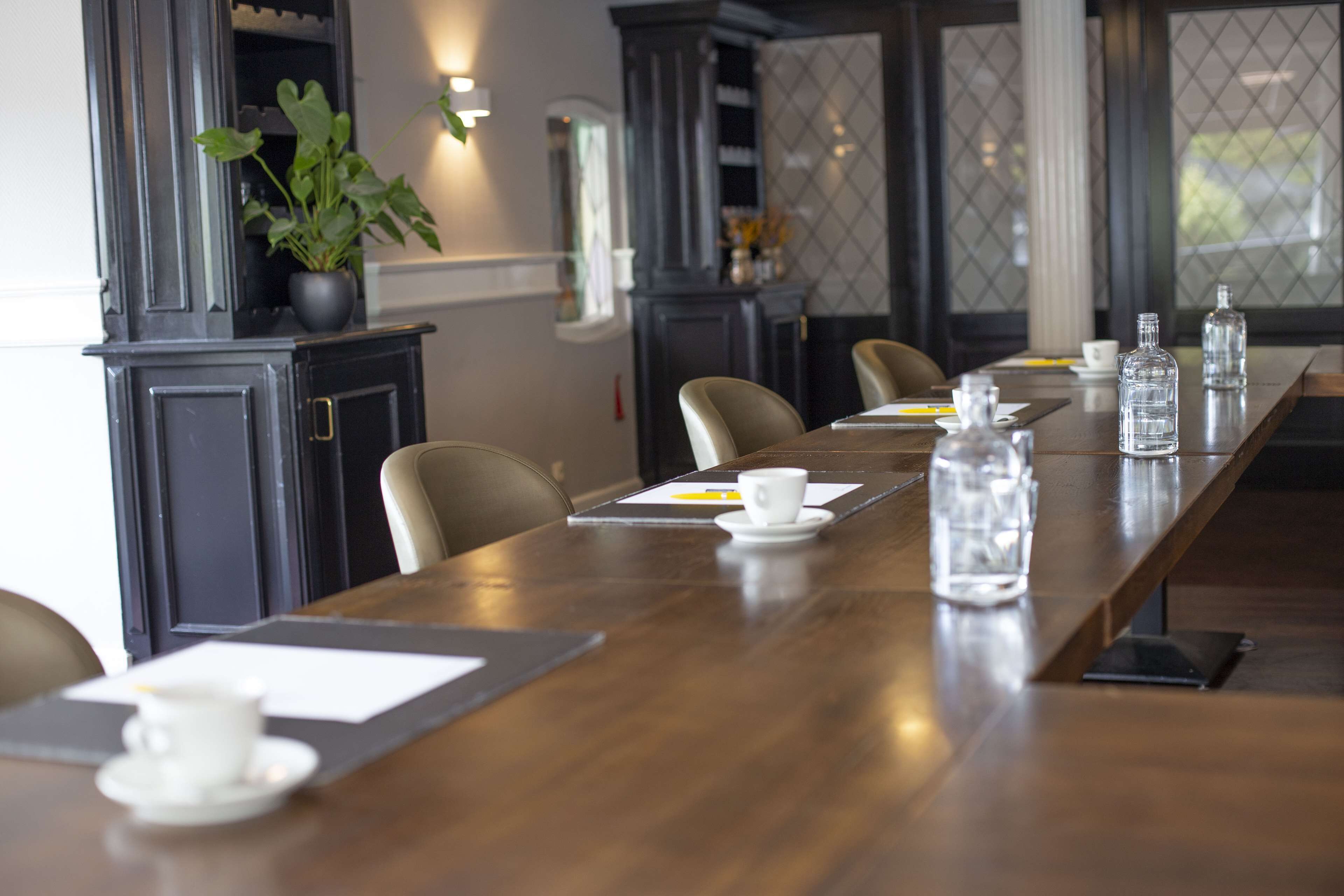 A conference room with a long wooden table, chairs, and a potted plant.
