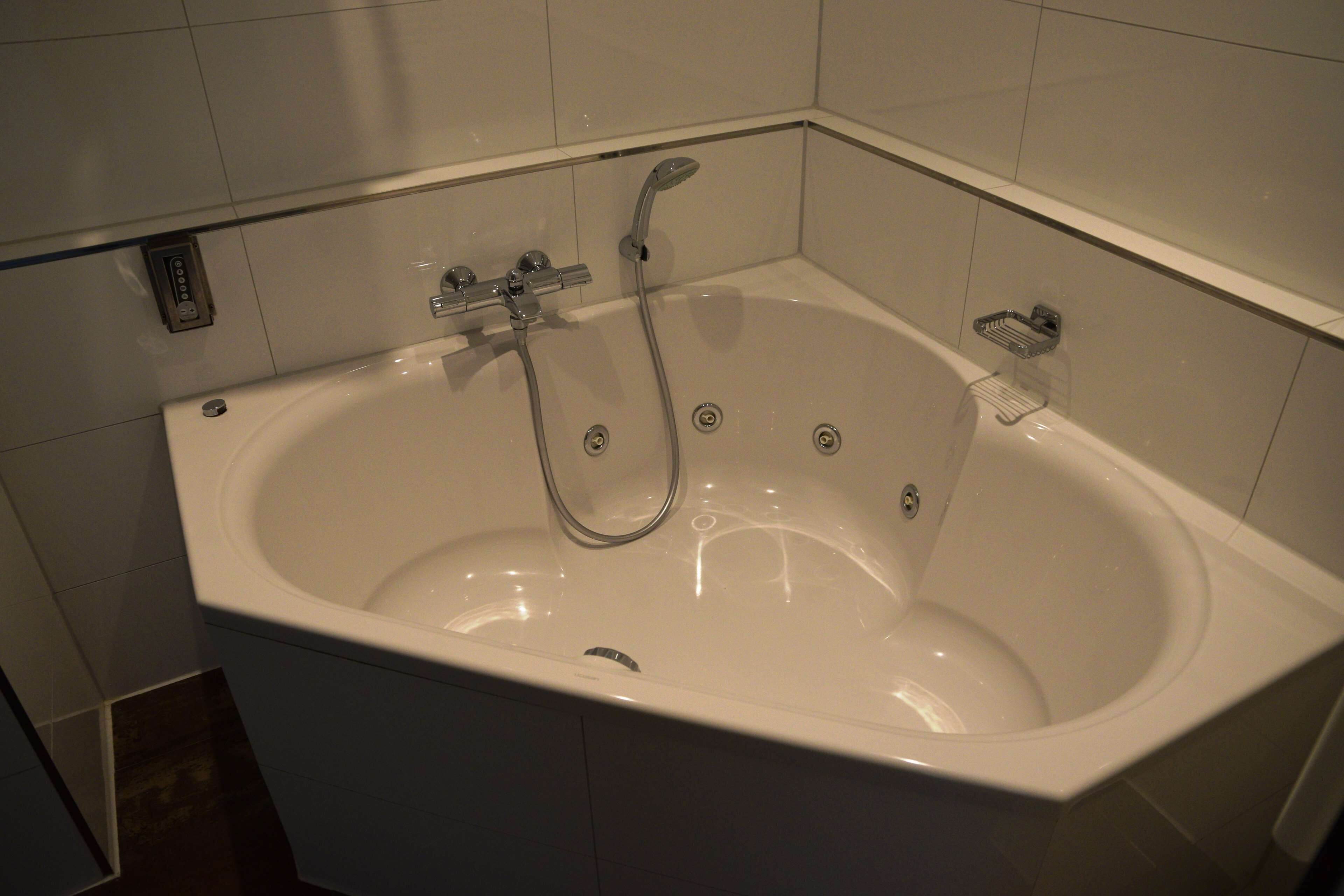 A white bathtub with a handheld showerhead, a built-in seat, and a small shelf.