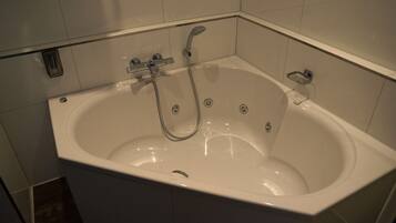 A white bathtub with a handheld showerhead, a built-in seat, and a small shelf.