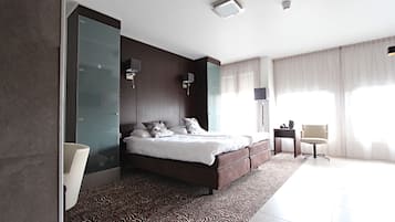 A modern bedroom with a large bed, a glass partition wall, a small bedside table, and a chair.