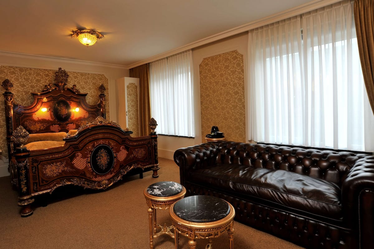Ein Zimmer mit einem großen, verzierten Bett, einem Ledersofa und zwei kleinen, runden Tischen.