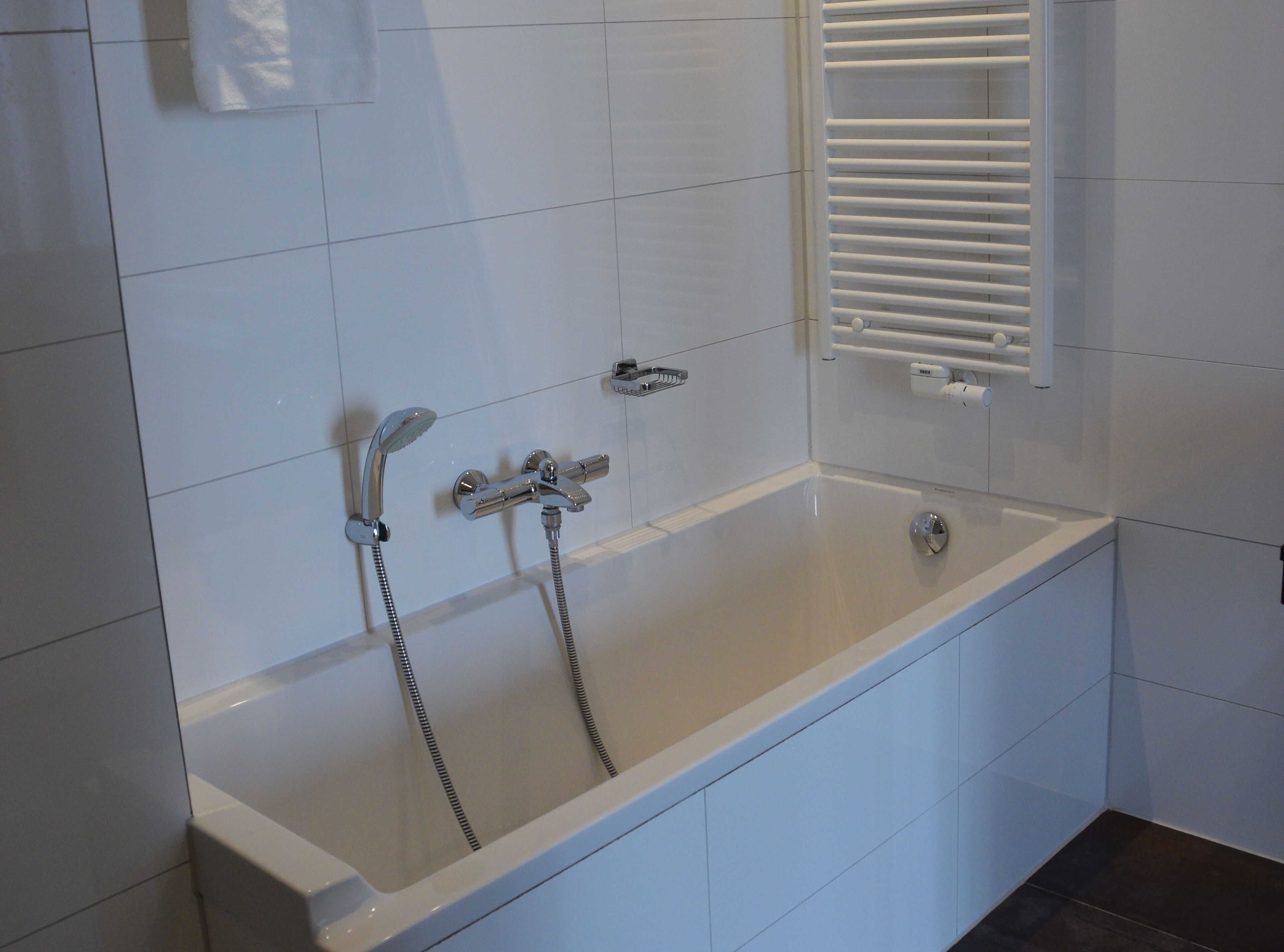 A modern bathroom with a white bathtub, a showerhead, and a towel rack.