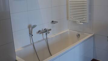 A modern bathroom with a white bathtub, a showerhead, and a towel rack.