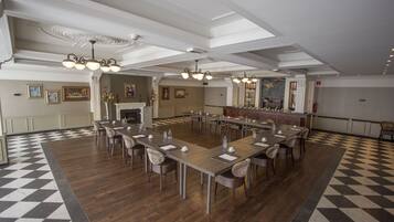 Een ruime congreszaal met een zwart-wit schakeerd vloer, meerdere tafels en stoelen.