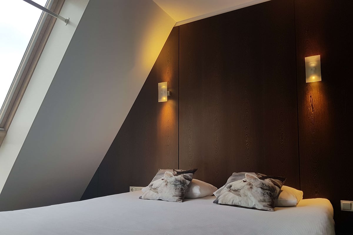 Ein modernes Schlafzimmer mit schrägen Wänden, einem großen Bett mit weißer Bettwäsche und zwei Wandleuchten.