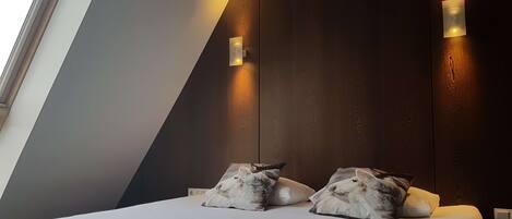 A modern bedroom with a sloped ceiling, a large bed with white bedding, and two wall-mounted light fixtures.
