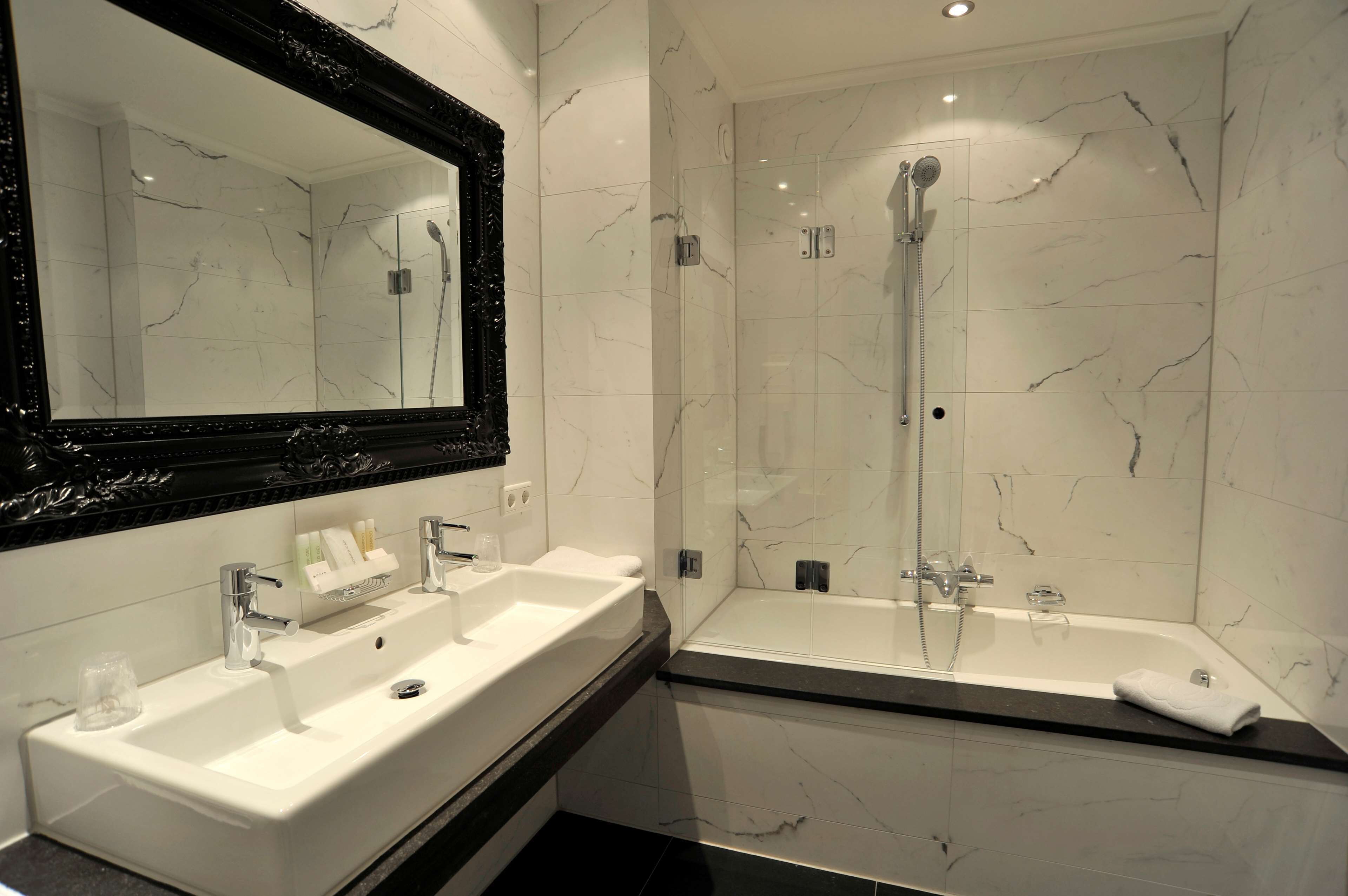 A modern bathroom with a large mirror, two sinks, a bathtub, and a glass-enclosed shower.